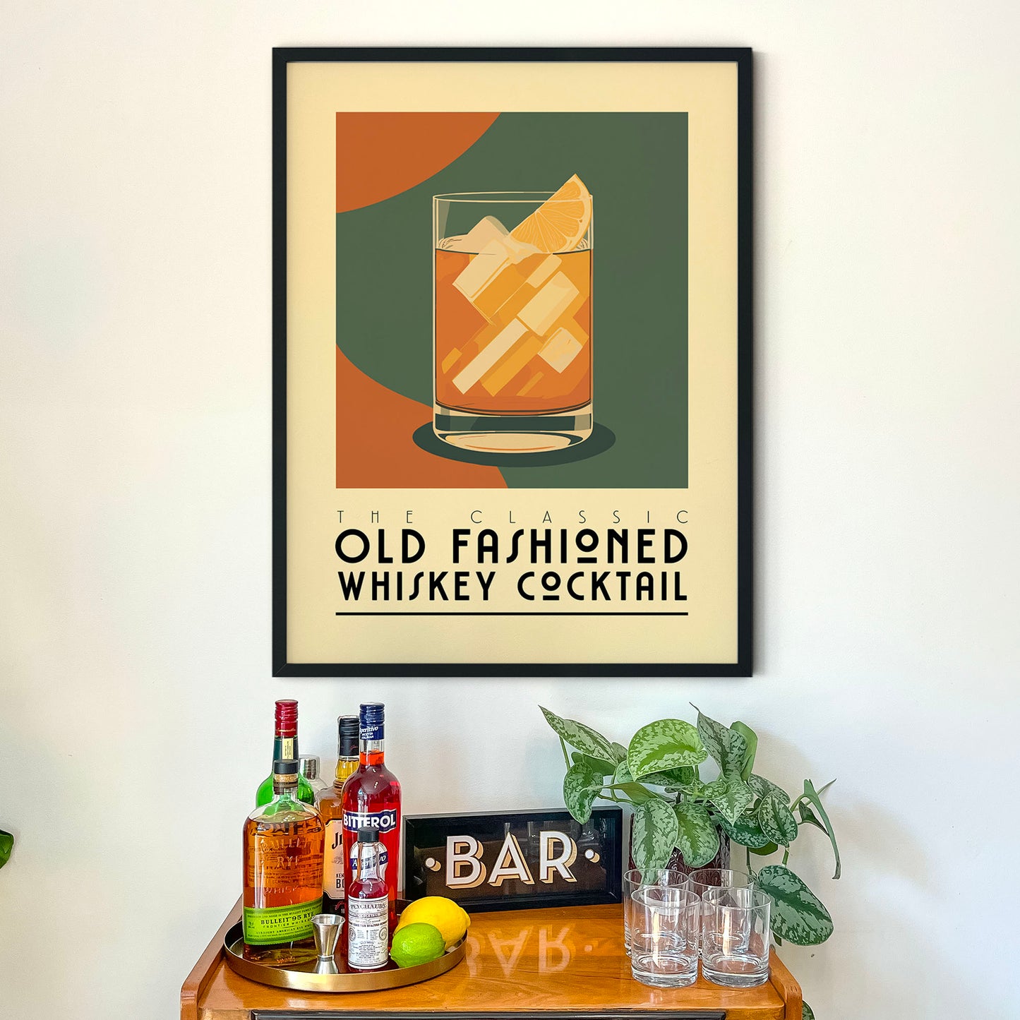 a framed poster of a whiskey cocktail on a wall above a wooden bar cart with various liquor bottles and glasses.