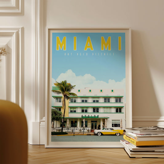 A framed poster of the Art Deco District in Miami, Florida, featuring a yellow and green building with palm trees and a yellow taxi in the foreground.