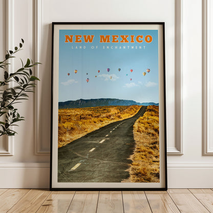 A framed poster of a desert road with hot air balloons in the sky, depicting the scenic landscape of New Mexico.