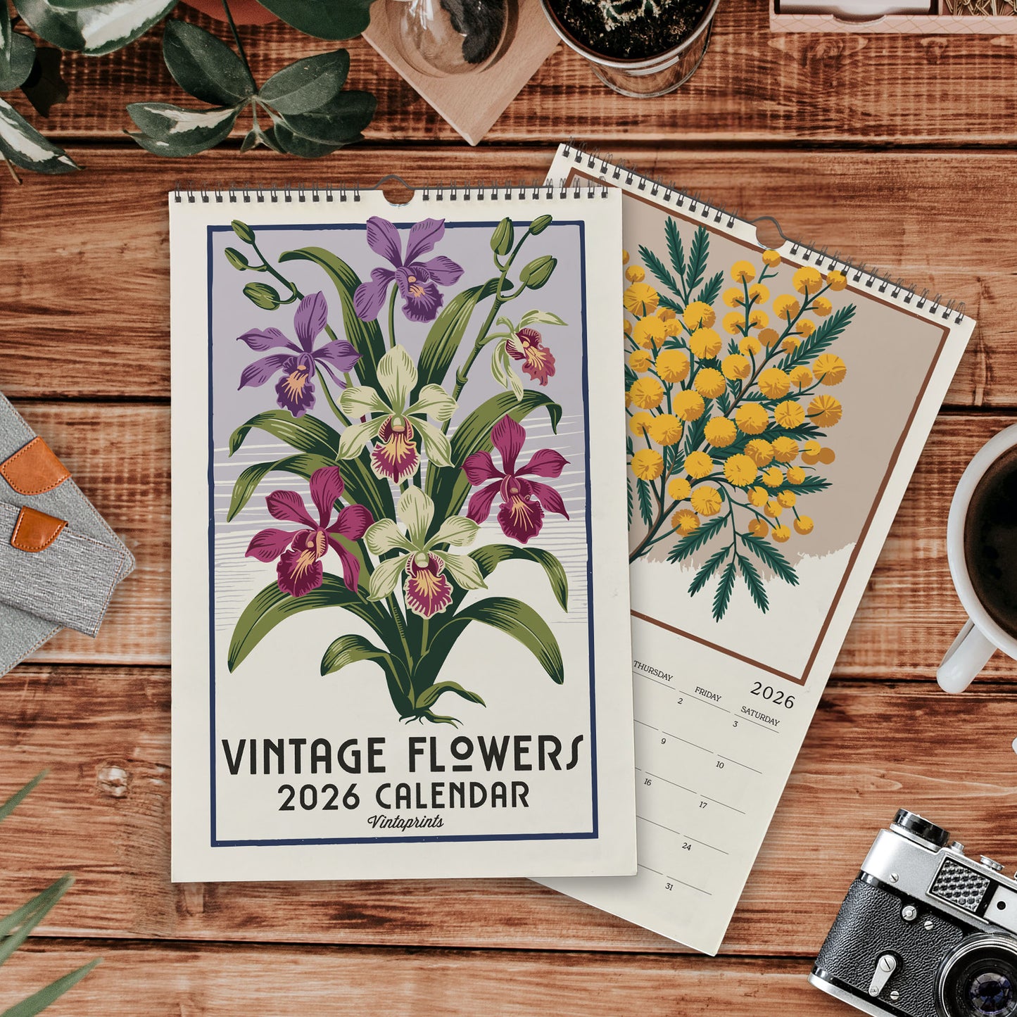a vintage-style flower calendar with a floral design, placed on a wooden surface alongside other items such as a camera, a mug, and some plants.
