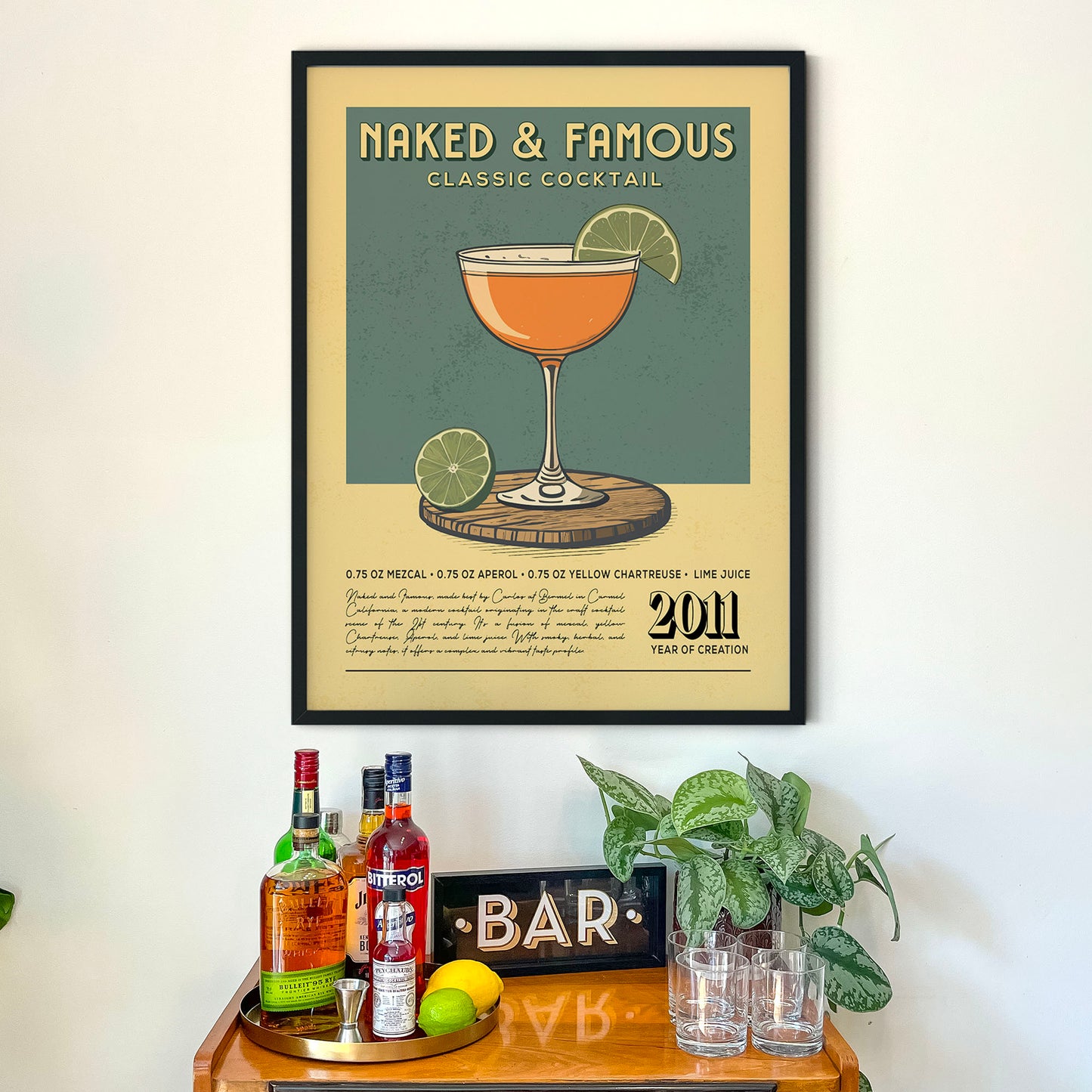 a framed poster of a classic cocktail, with a wooden tray below it containing various bottles of alcohol and glasses.