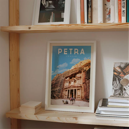A framed poster of Petra, a famous ancient archaeological site in Jordan, is displayed on a shelf among other books and items.