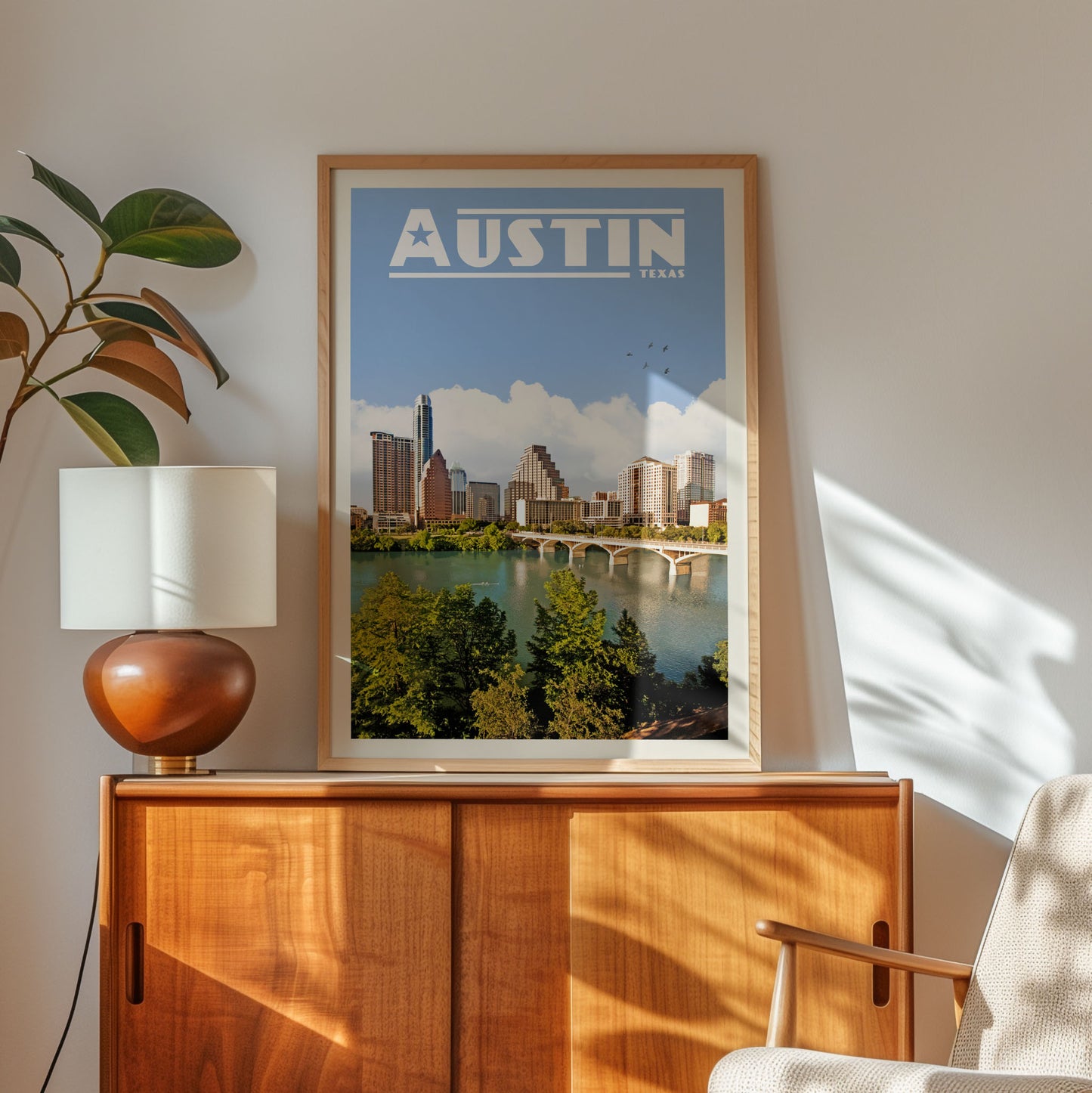 a framed poster of the Austin skyline, with a cityscape of buildings and a river in the background, hanging on a wall above a wooden cabinet.