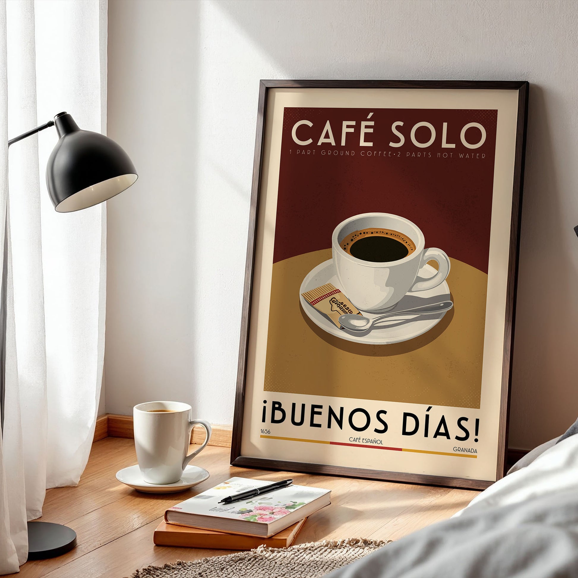a framed poster of a cup of coffee on a table, with a lamp and a book nearby.