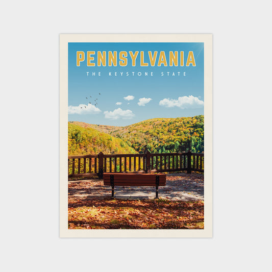 A scenic view of a park bench overlooking a forested hillside with autumn foliage, set against a clear blue sky with a few birds in flight.