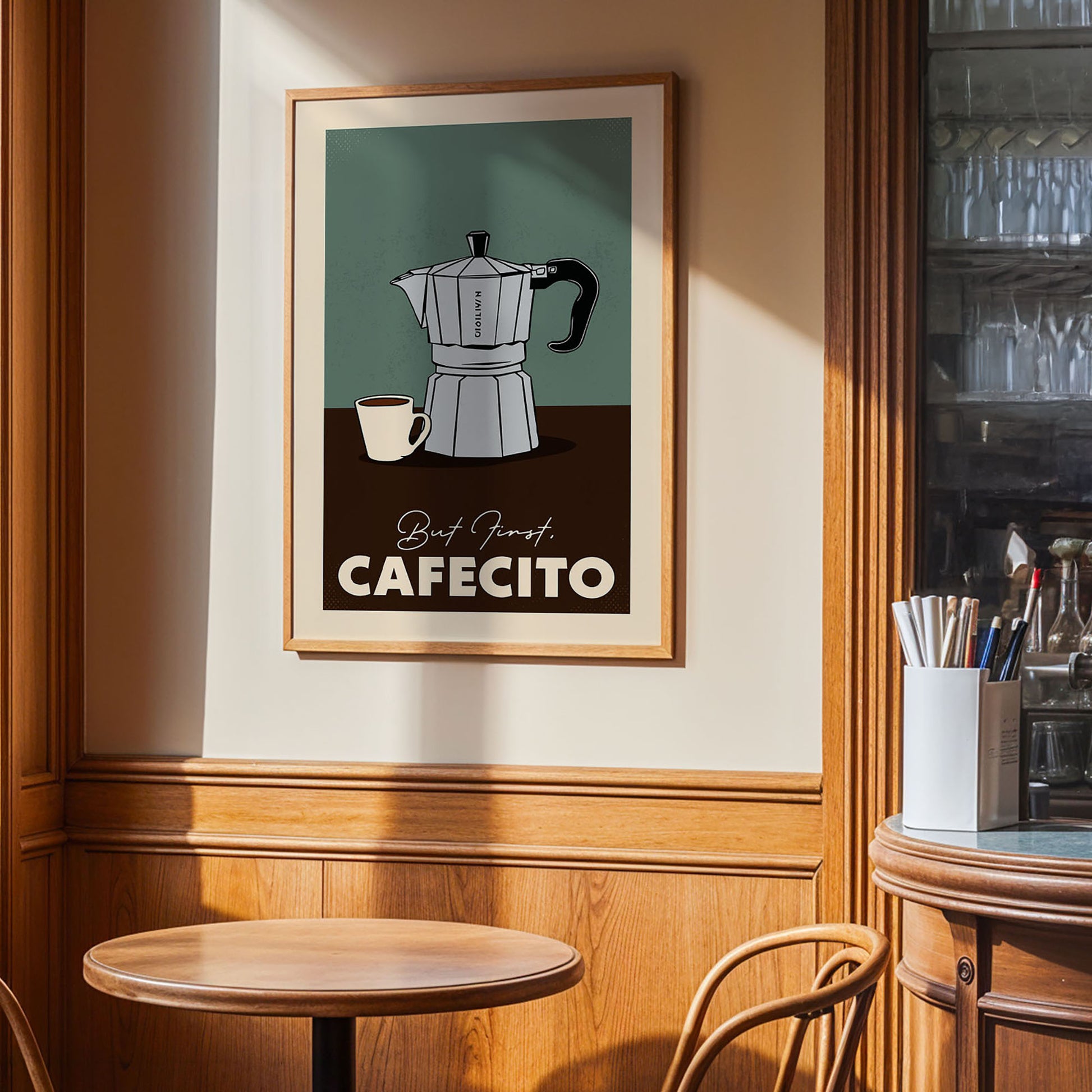 a framed poster of a coffee maker and a cup of coffee on a wooden table, with the text "Best First CAFECITO" displayed on the poster.