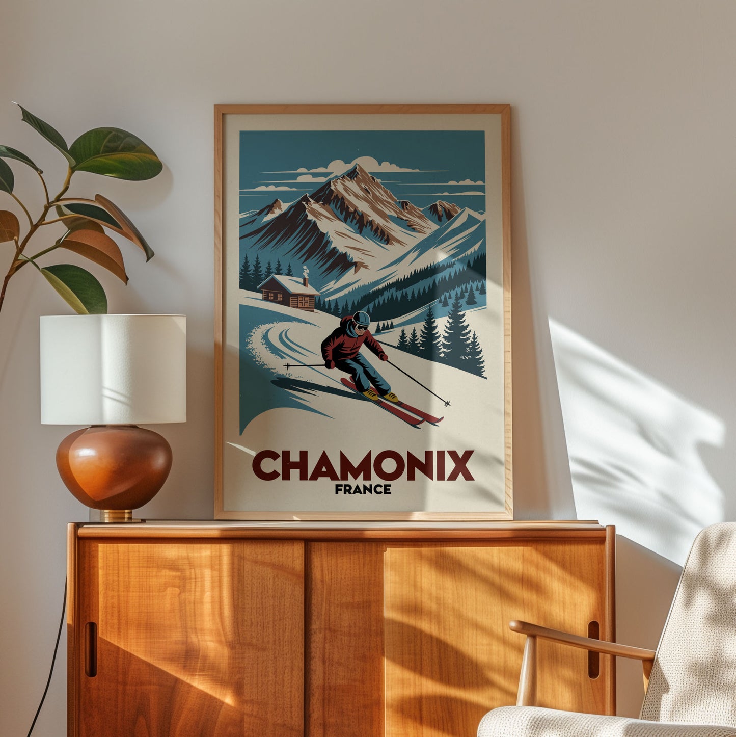 a framed poster of a skier on a snowy mountain, with the word "CHAMONIX" written below the skier. The poster is displayed on a wooden cabinet, and there is a lamp and a plant in the foreground.