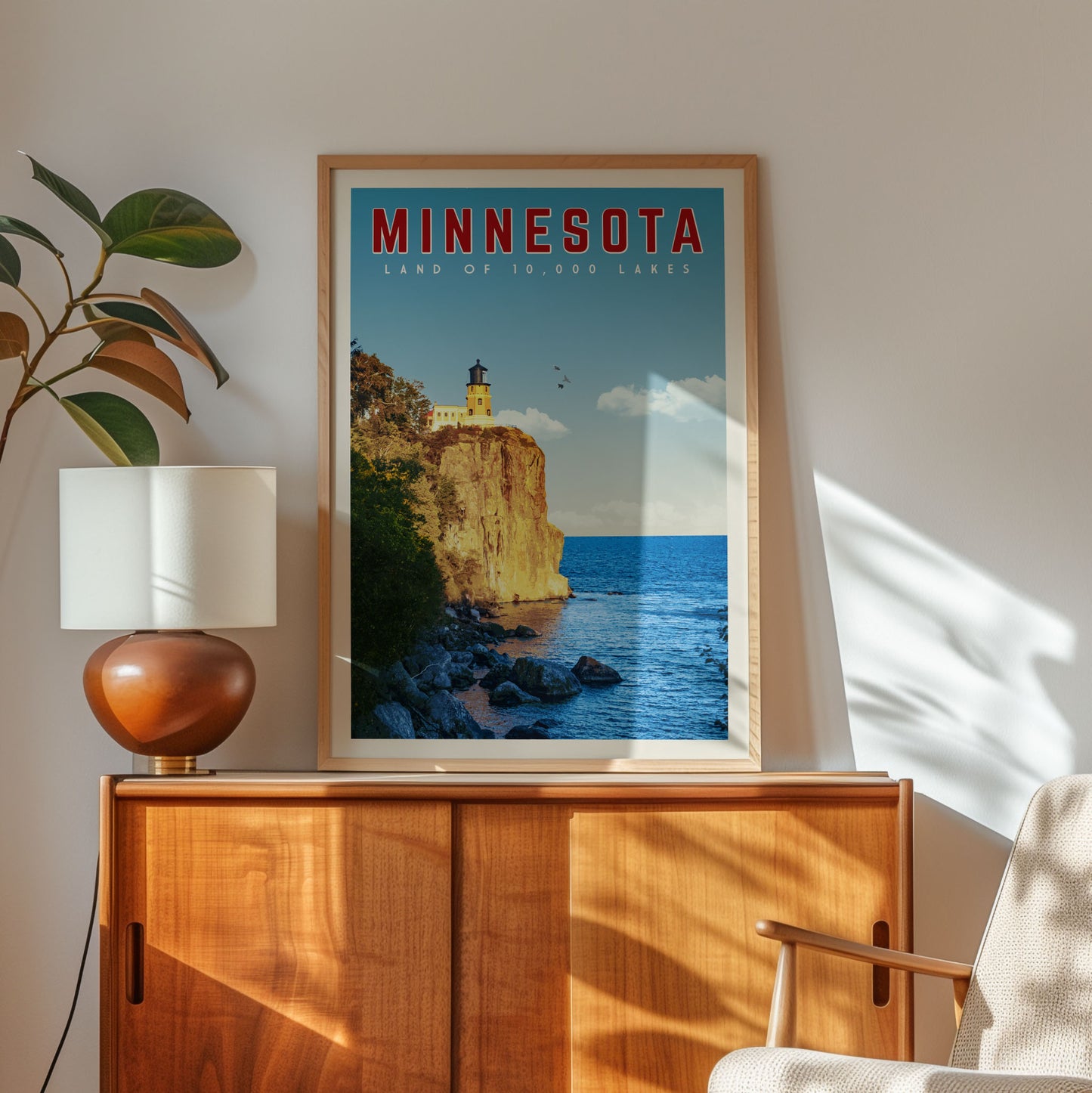 A framed poster of a scenic view of Minnesota's Land of 10,000 Lakes hangs on a wooden cabinet in a room with a lamp and a plant.