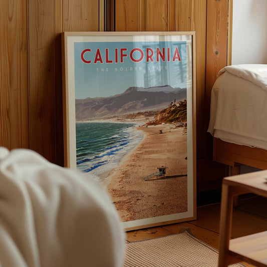 A framed poster of a beach scene in California, with mountains in the background.
