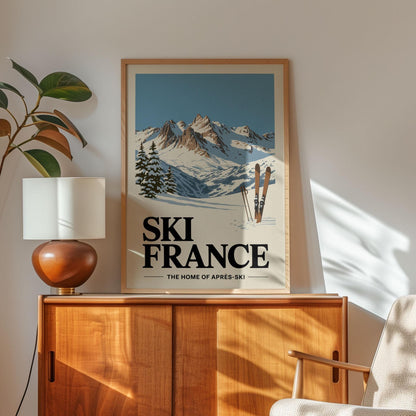 a framed poster of a snowy mountain landscape with skis, placed on a wooden cabinet or shelf.