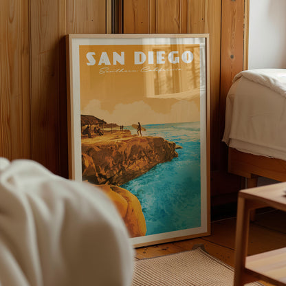 A framed poster of a beach scene with a surfer on a cliff overlooking the ocean, located in a room with wooden walls.