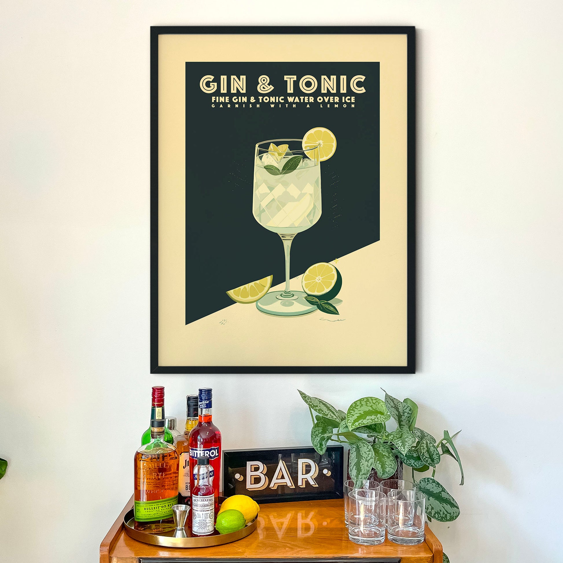 a framed poster of a gin and tonic drink on a wall above a wooden bar cart with various liquor bottles and glasses.