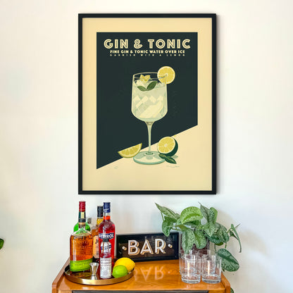 a framed poster of a gin and tonic drink on a wall above a wooden bar cart with various liquor bottles and glasses.