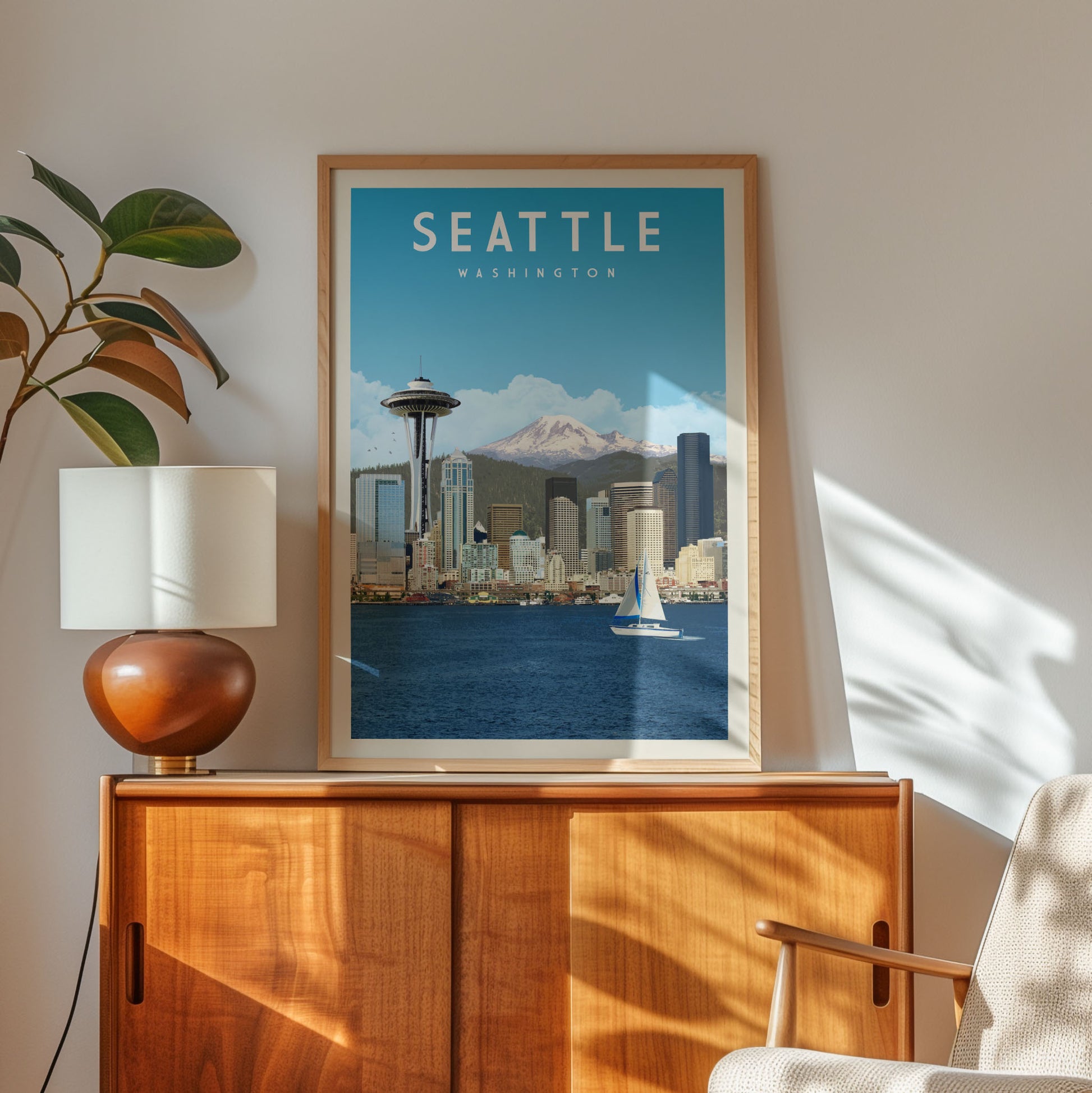 a framed poster of the Seattle skyline, with a mountain in the background and a sailboat on the water. The poster is hanging on a wall, and there is a lamp and a wooden cabinet below it.