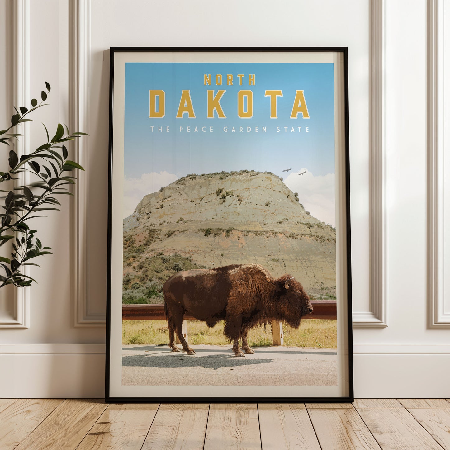 A framed poster of a buffalo standing on a road in front of a mountain, with the text "NORTH DAKOTA THE PEACE GARDEN STATE" displayed prominently.