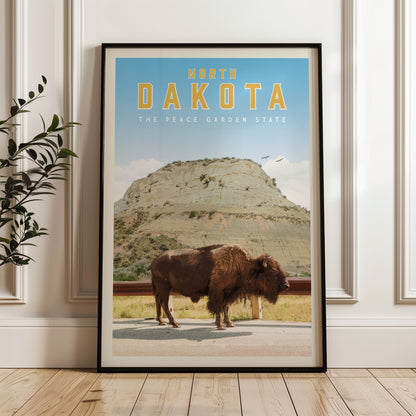 A framed poster of a buffalo standing on a road in front of a mountain, with the text "NORTH DAKOTA THE PEACE GARDEN STATE" displayed prominently.