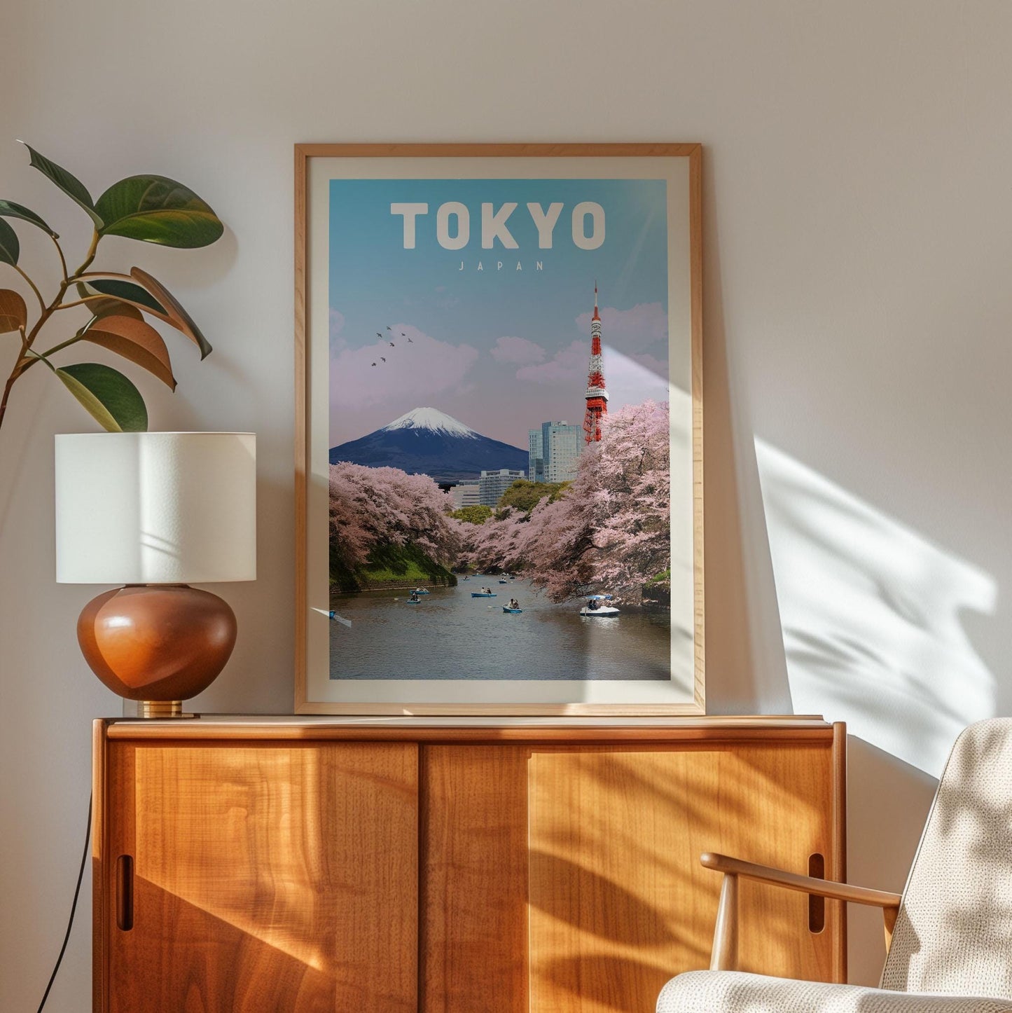a framed poster of Tokyo, Japan, with a view of the Tokyo Tower and cherry blossom trees, placed on a wooden cabinet.