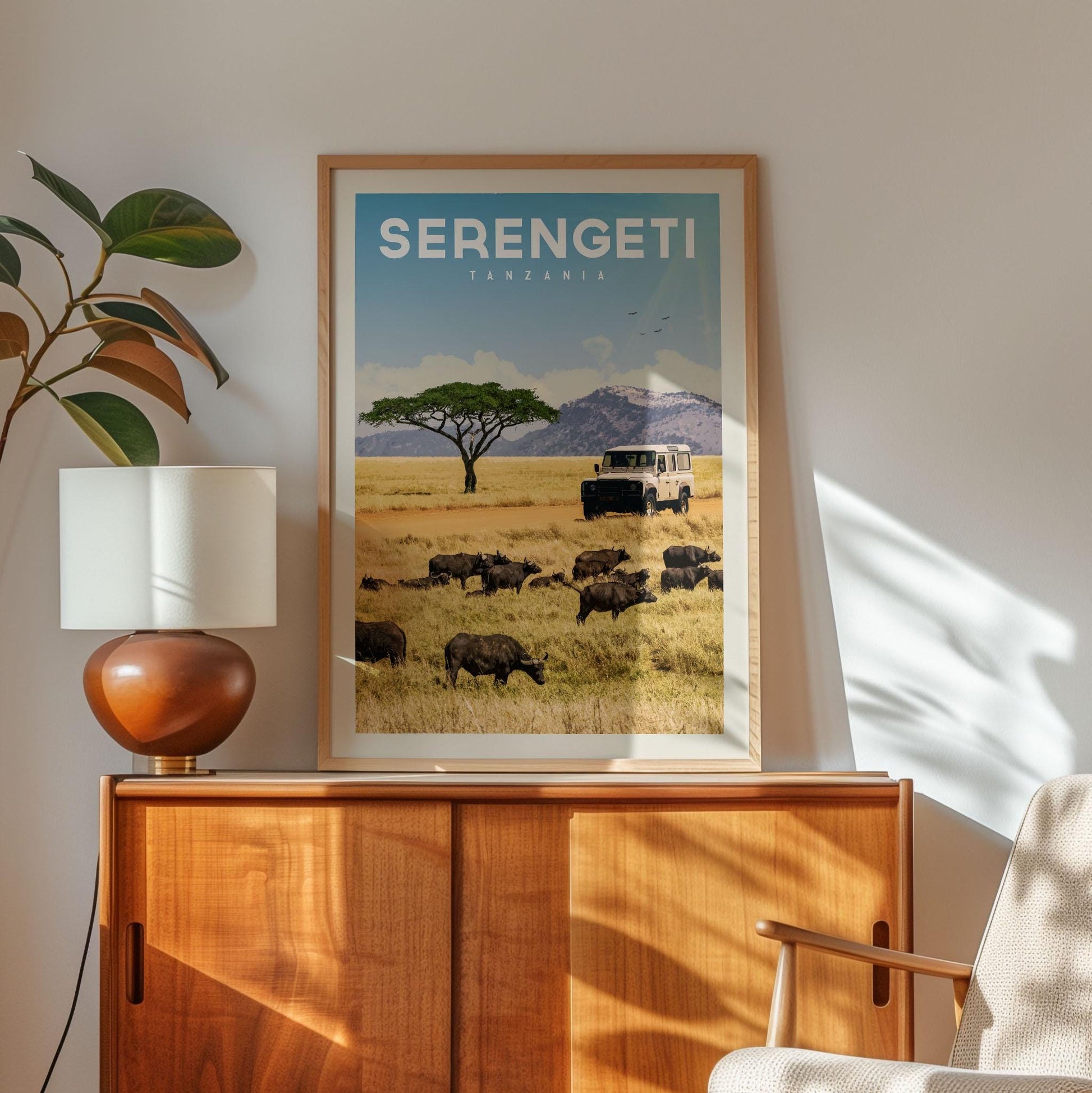 a framed poster of a safari scene with a herd of animals in the foreground and a safari vehicle in the background, set against a backdrop of a grassy field and mountains.