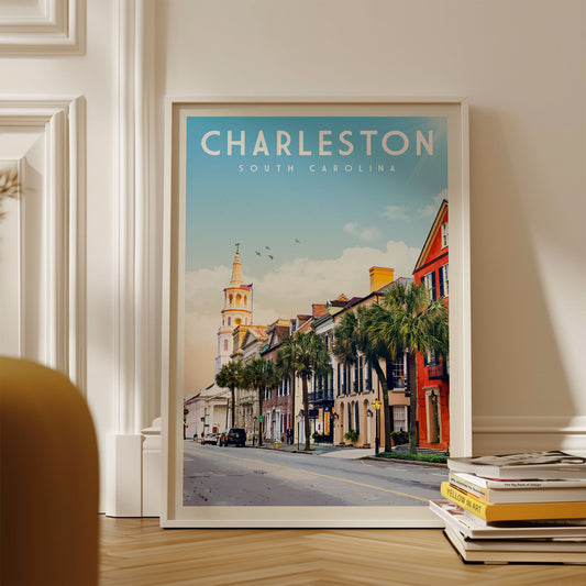 A framed poster of a street scene in Charleston, South Carolina, with a church steeple and colorful buildings in the background.
