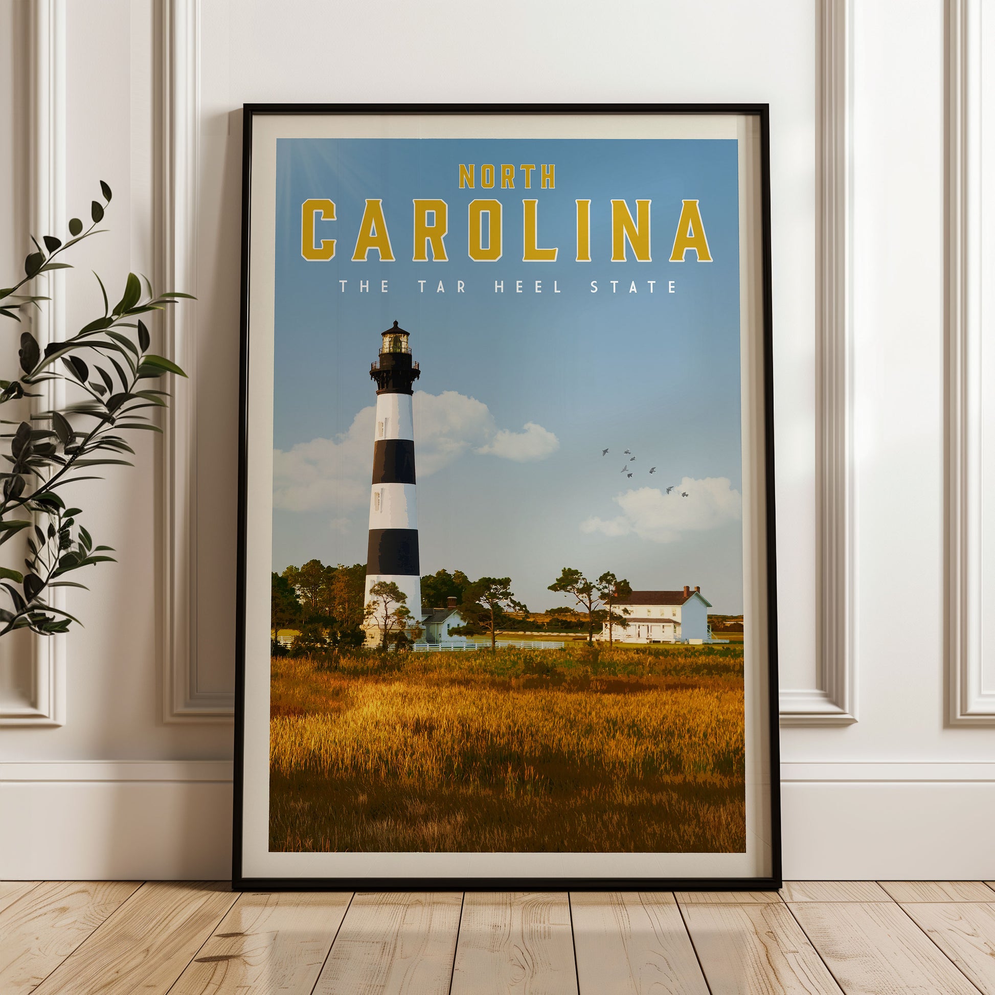 A framed poster of a lighthouse in North Carolina, with a clear blue sky and a grassy field in the background.