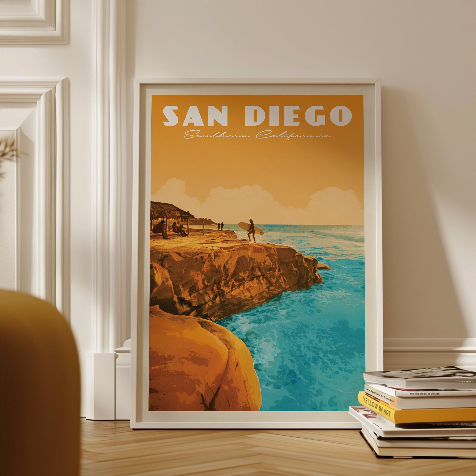 A framed poster of a scenic coastal landscape with a surfer on a rocky cliff overlooking the ocean, displayed on a wall.