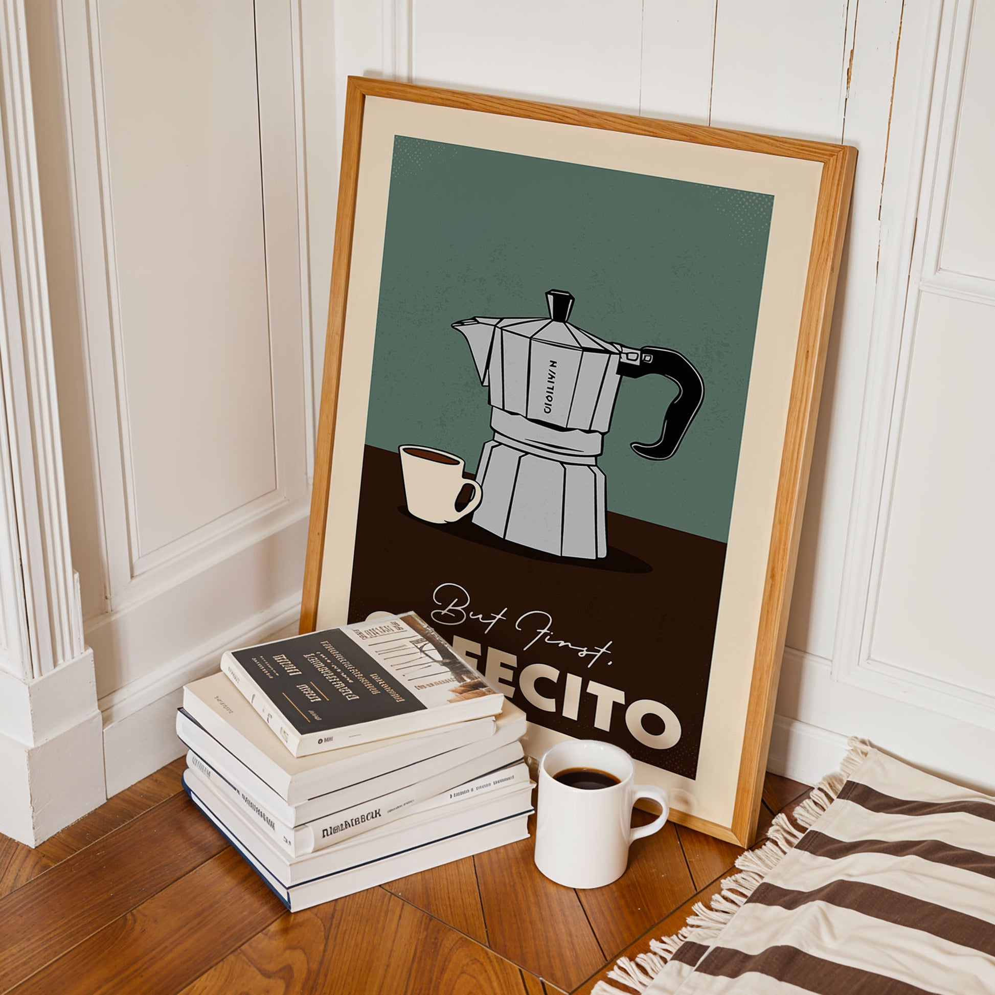 A framed poster of a coffee maker is leaning against a white wall, with a stack of books and a cup of coffee nearby.