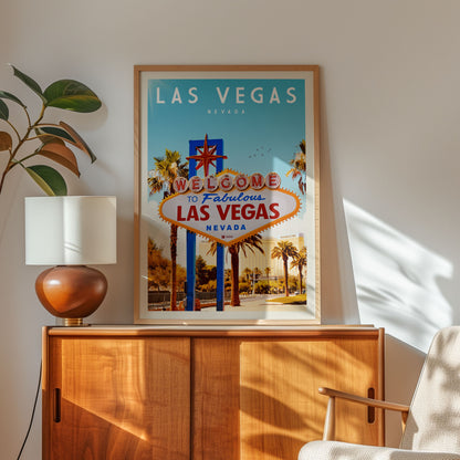 a framed poster of the Las Vegas sign, which is a popular tourist attraction in Nevada. The poster displays the words "Welcome to Fabulous Las Vegas" and " Nevada" in bold letters, inviting viewers to explore the city. The poster is hung on a wall, and there is a lamp and a plant nearby, creating a cozy and welcoming atmosphere.