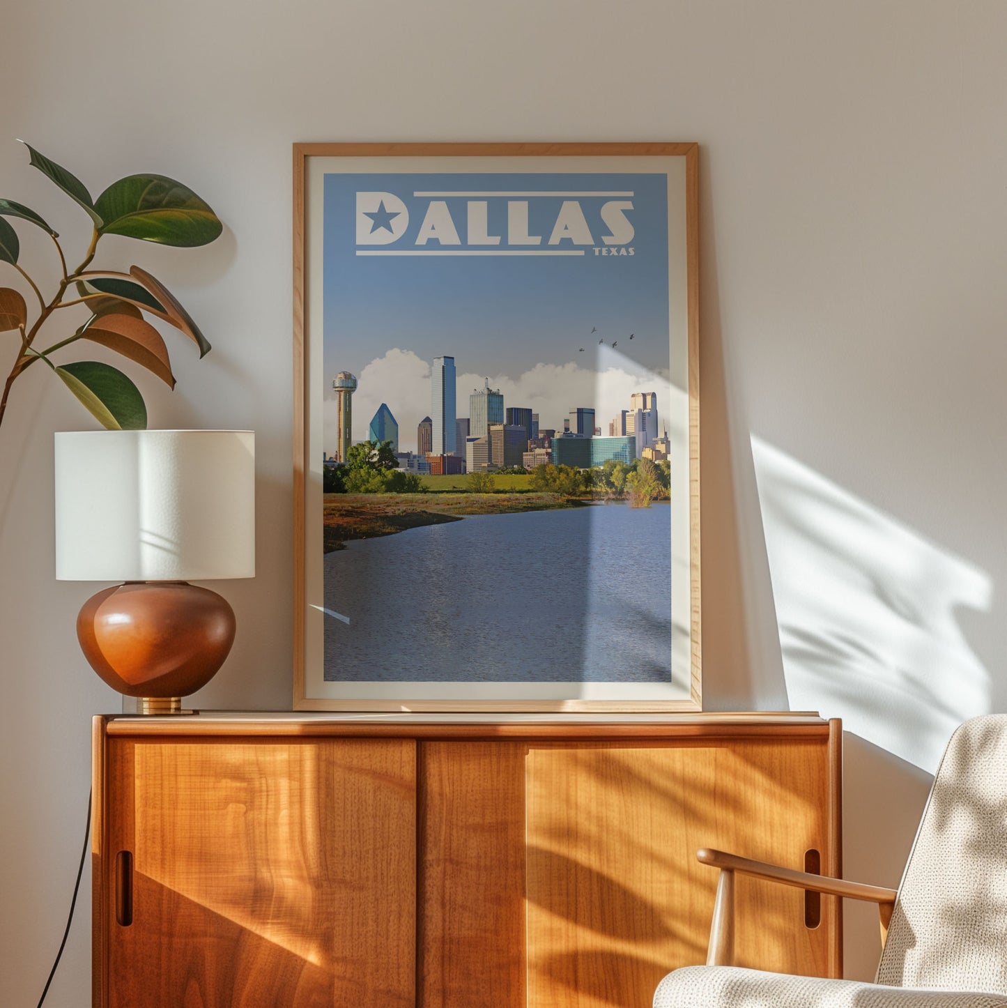 a framed poster of the Dallas skyline, with a lamp and a wooden cabinet below it.