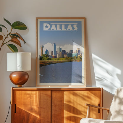 a framed poster of the Dallas skyline, with a lamp and a wooden cabinet below it.