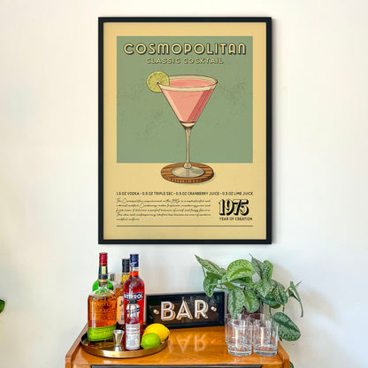 a framed poster of a cocktail glass with a pink drink, placed above a wooden bar counter with various liquor bottles and glasses.