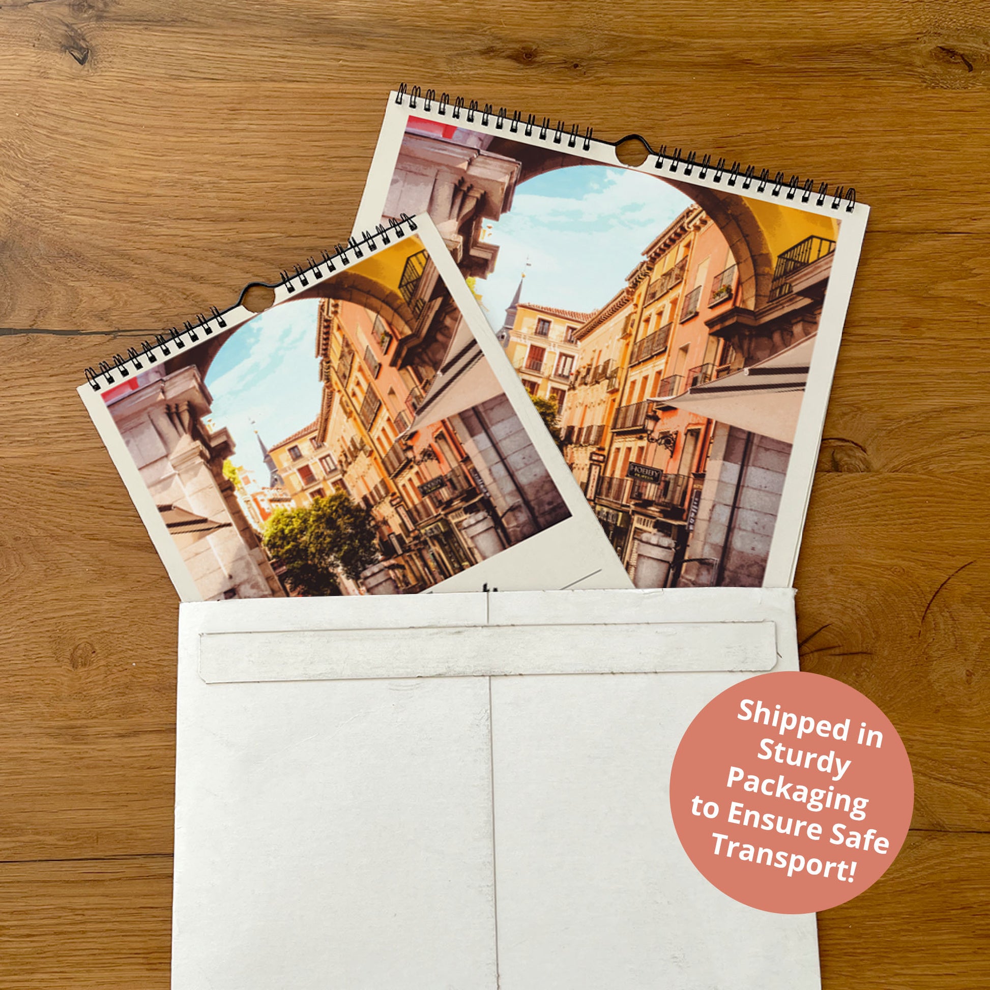 two spiral-bound photo albums placed inside a white envelope on a wooden surface.