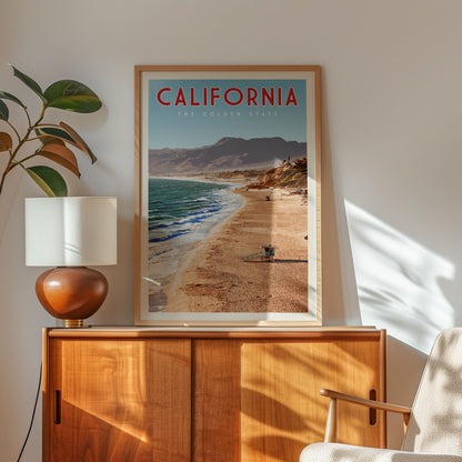 a framed poster of a beach scene with mountains in the background, hanging on a wall next to a wooden cabinet and a lamp.