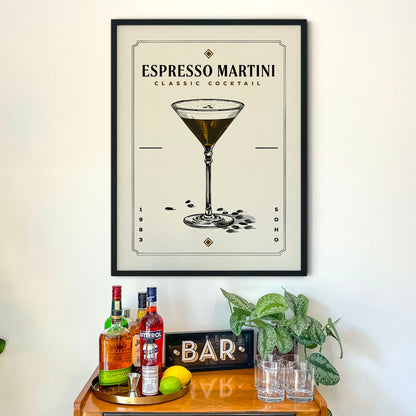 a framed poster of an espresso martini cocktail hanging on a wall above a wooden bar cart. The poster displays an illustration of the cocktail glass and the word "ESPRESSO MARTINI" along with the text "CLASSIC COCKTAIL". The bar cart is filled with various liquor bottles and has a sign that reads "BAR".