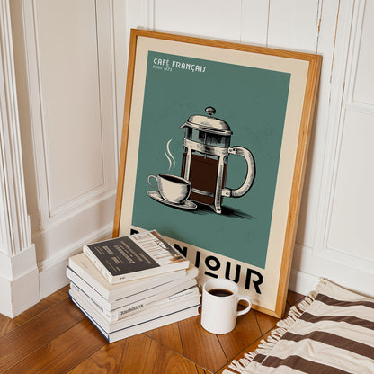 a framed poster of a French press coffee maker, a stack of books, and a white mug on a wooden floor.