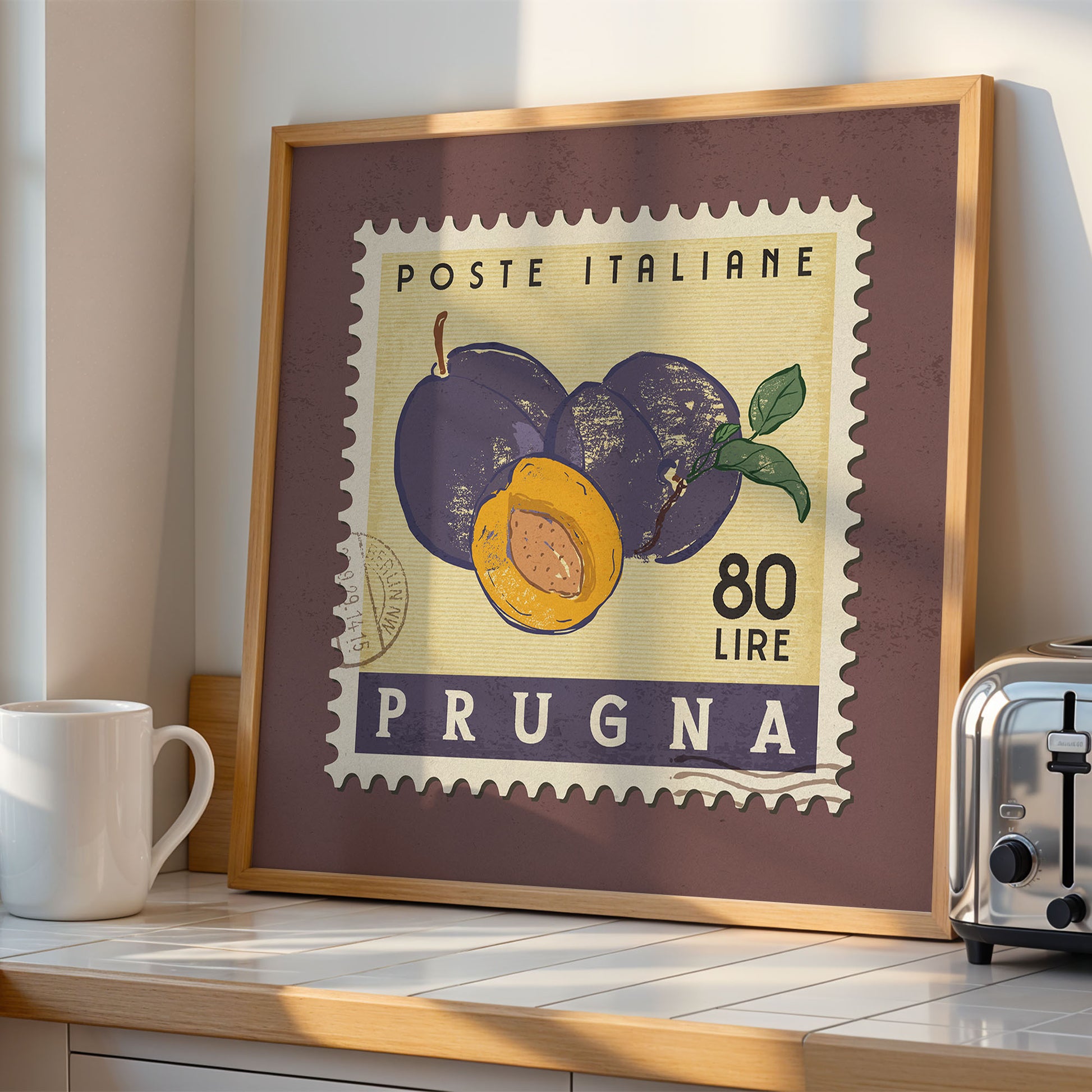 a framed stamp-like artwork depicting plums and a toaster on a kitchen counter.