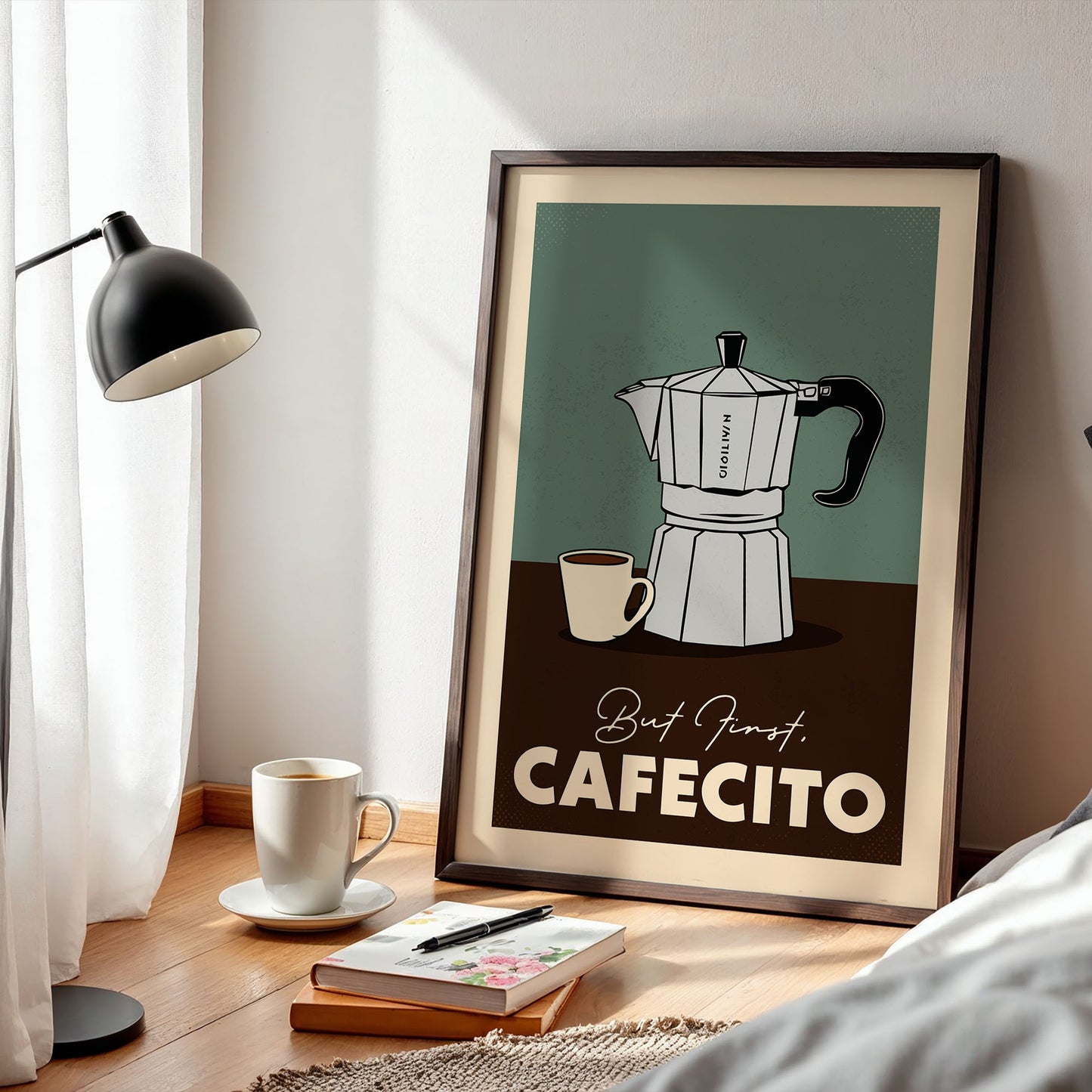 A framed poster of a coffee maker is displayed on a wooden floor next to a lamp, a cup of coffee, and some books.