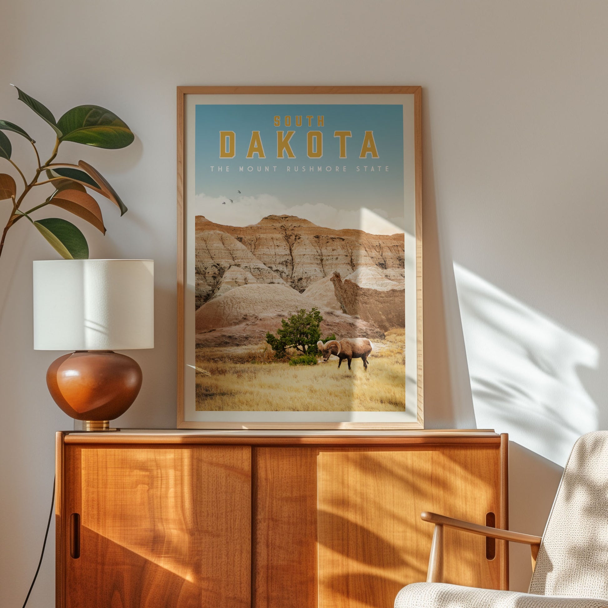 a framed poster of a scenic landscape with a mountain range and a lone tree, hanging on a wall above a wooden cabinet.