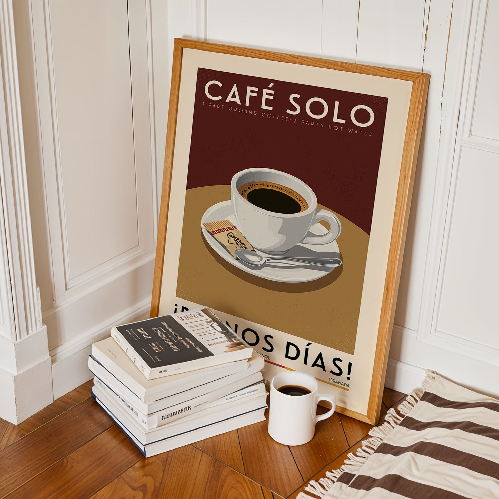 A framed poster of a cup of coffee on a table, surrounded by a stack of books and a white mug, all placed on a wooden floor.