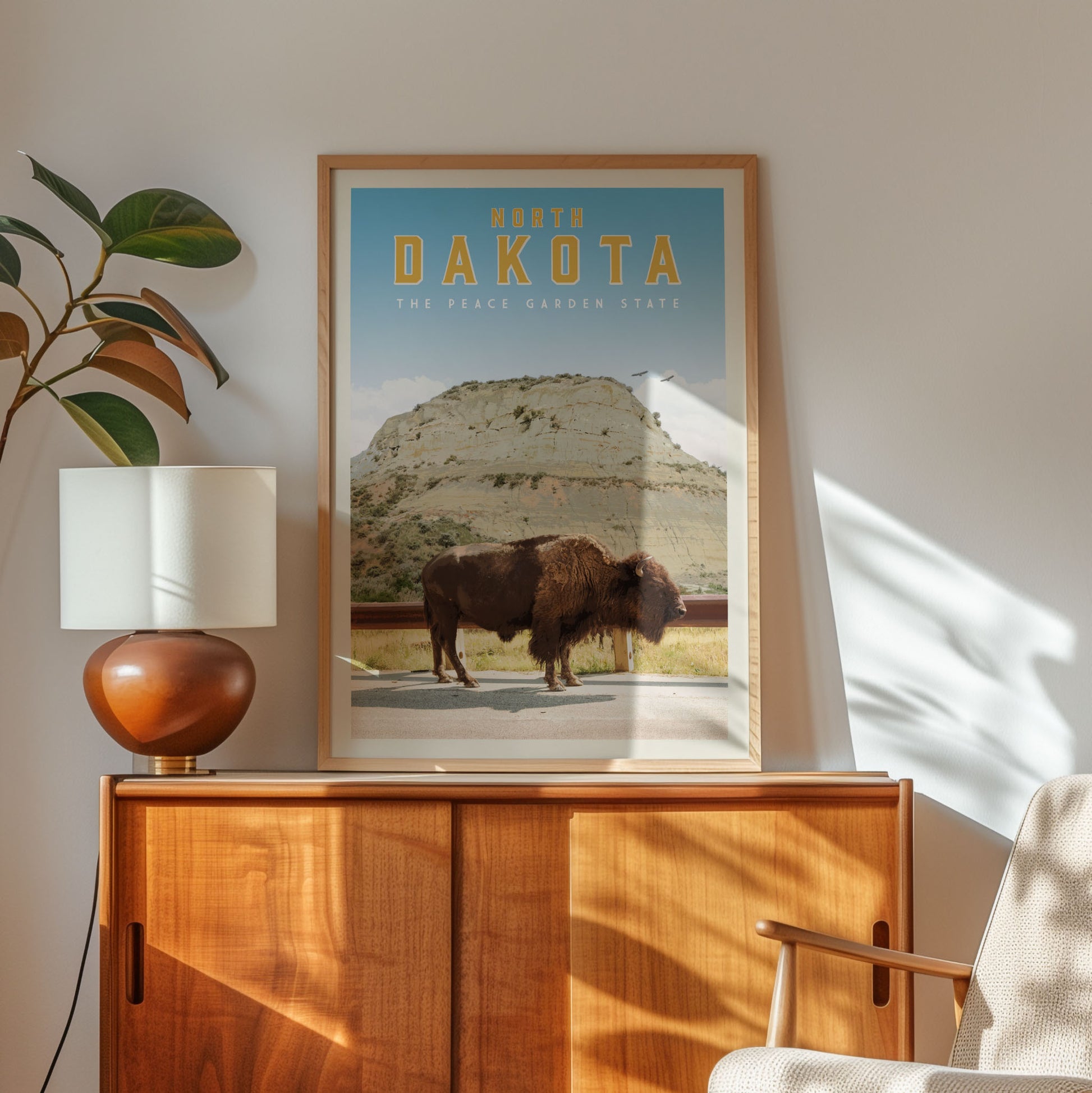 a framed poster of a buffalo on a wooden cabinet, with a lamp and a plant on the side.