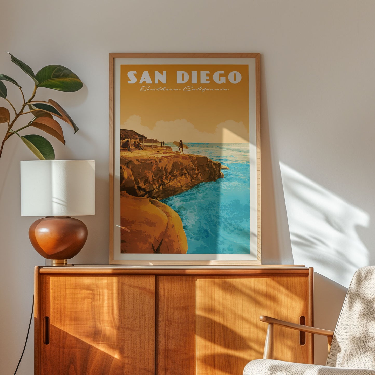 a framed poster of a scenic coastal landscape with a person standing on a cliff overlooking the ocean, placed on a wooden cabinet or dresser.