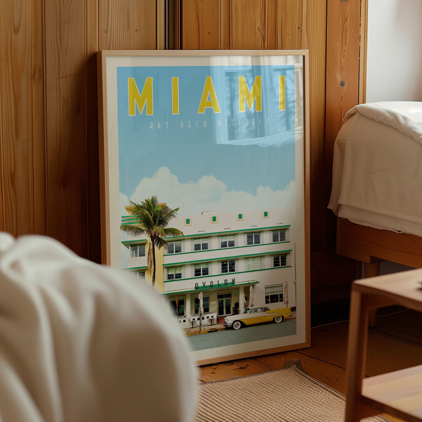 A framed poster of the Art Deco Hotel in Miami, Florida, with a palm tree and a yellow car in the foreground.