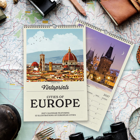a calendar with a photo of a city skyline, specifically Florence, Italy, on the cover. The calendar is titled "Vintaprints Cities of Europe" and includes a "2027 Calendar Featuring 12 Illustrations of European Cities" description. The calendar is placed on top of a map, and various travel-related items such as a camera, binoculars, and a wallet are also visible in the image.