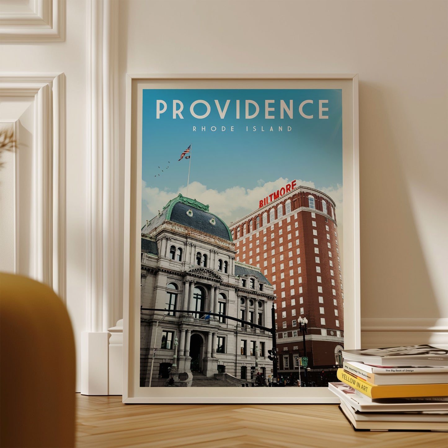 a framed poster of a cityscape with a large building and a smaller building, both with the word "Rothmore" written on them. The poster is displayed on a wall, and there are some books stacked nearby.