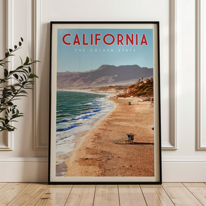 A framed poster of a beach scene in California, with mountains in the background and a lifeguard tower visible on the sandy shore.