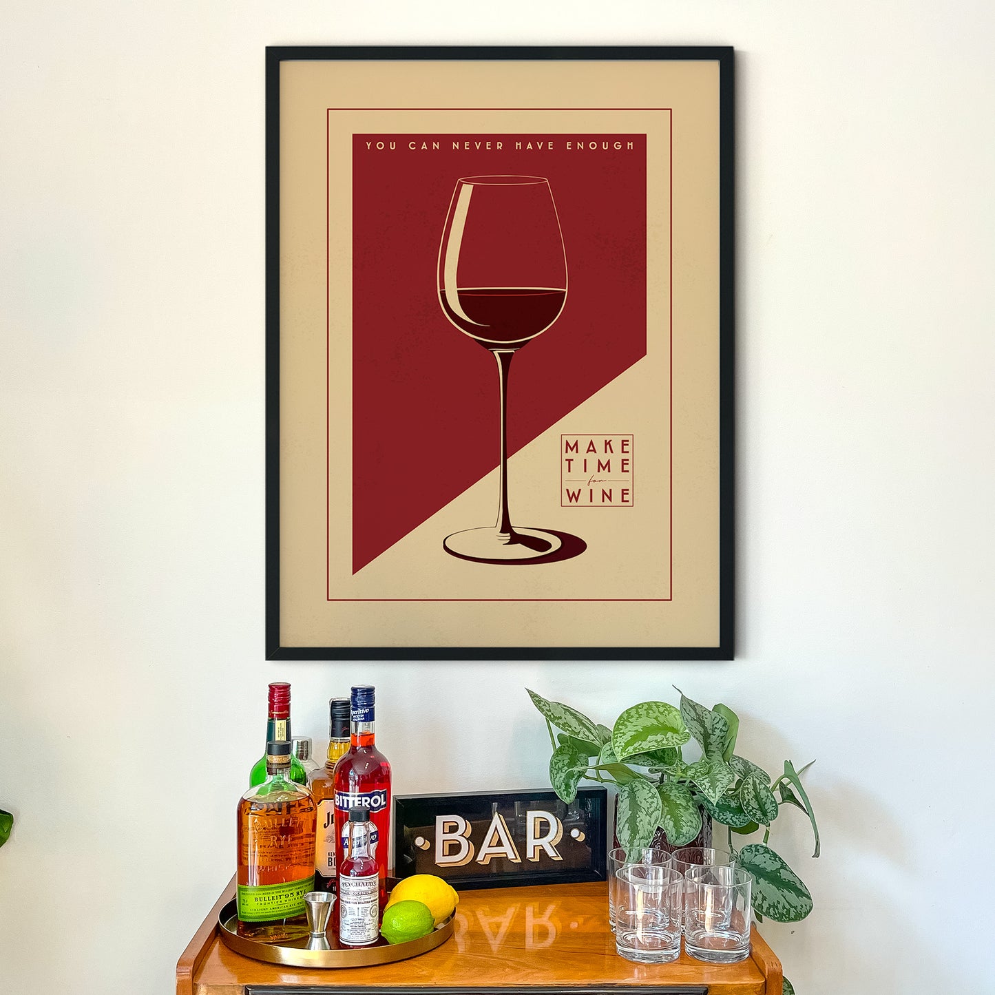 a framed poster with a wine glass illustration, accompanied by the text "You can never have enough wine" and "Make time for wine" on a wooden table below it.