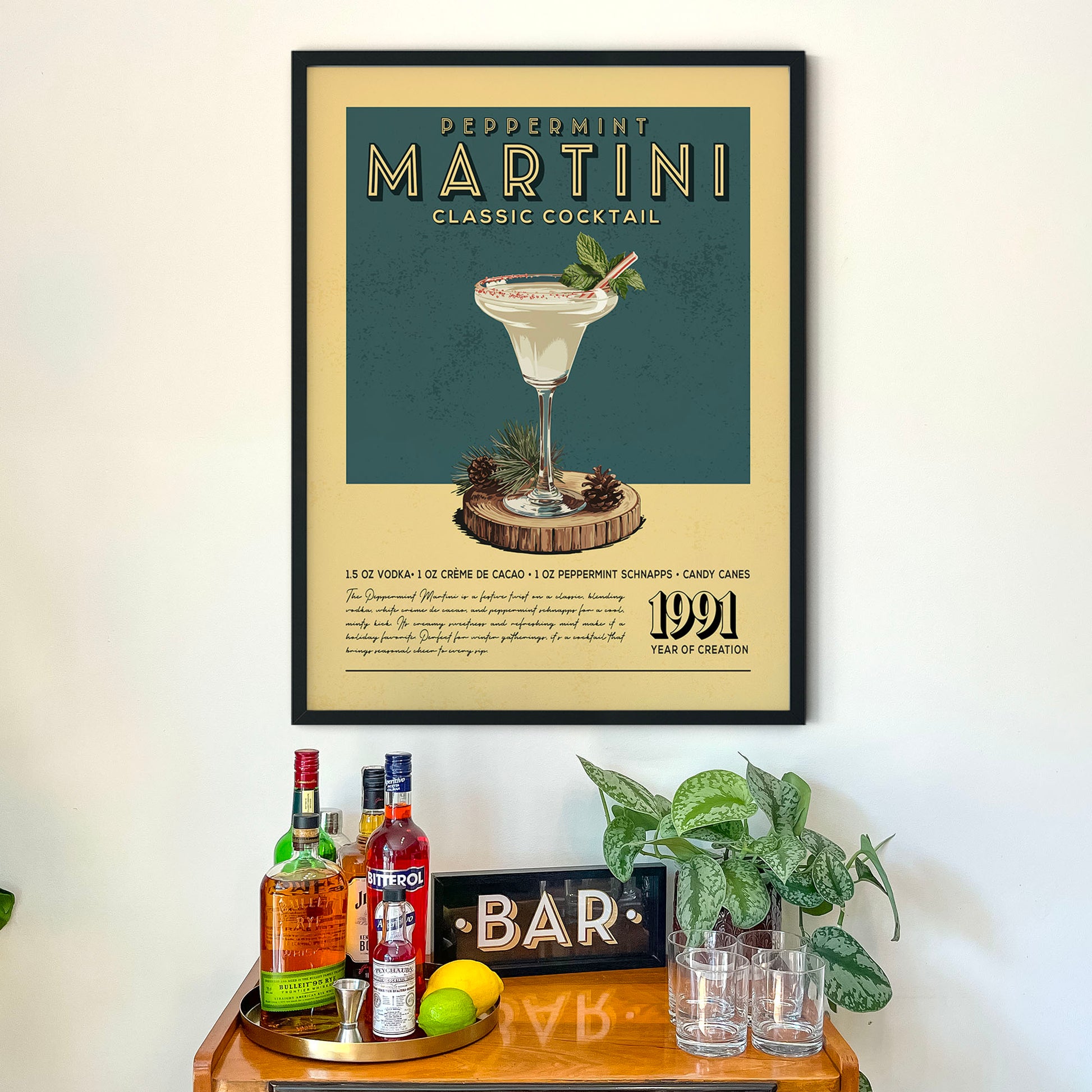 A framed poster of a classic martini cocktail hangs on a wall above a wooden bar counter, which has various liquor bottles and glasses on it.
