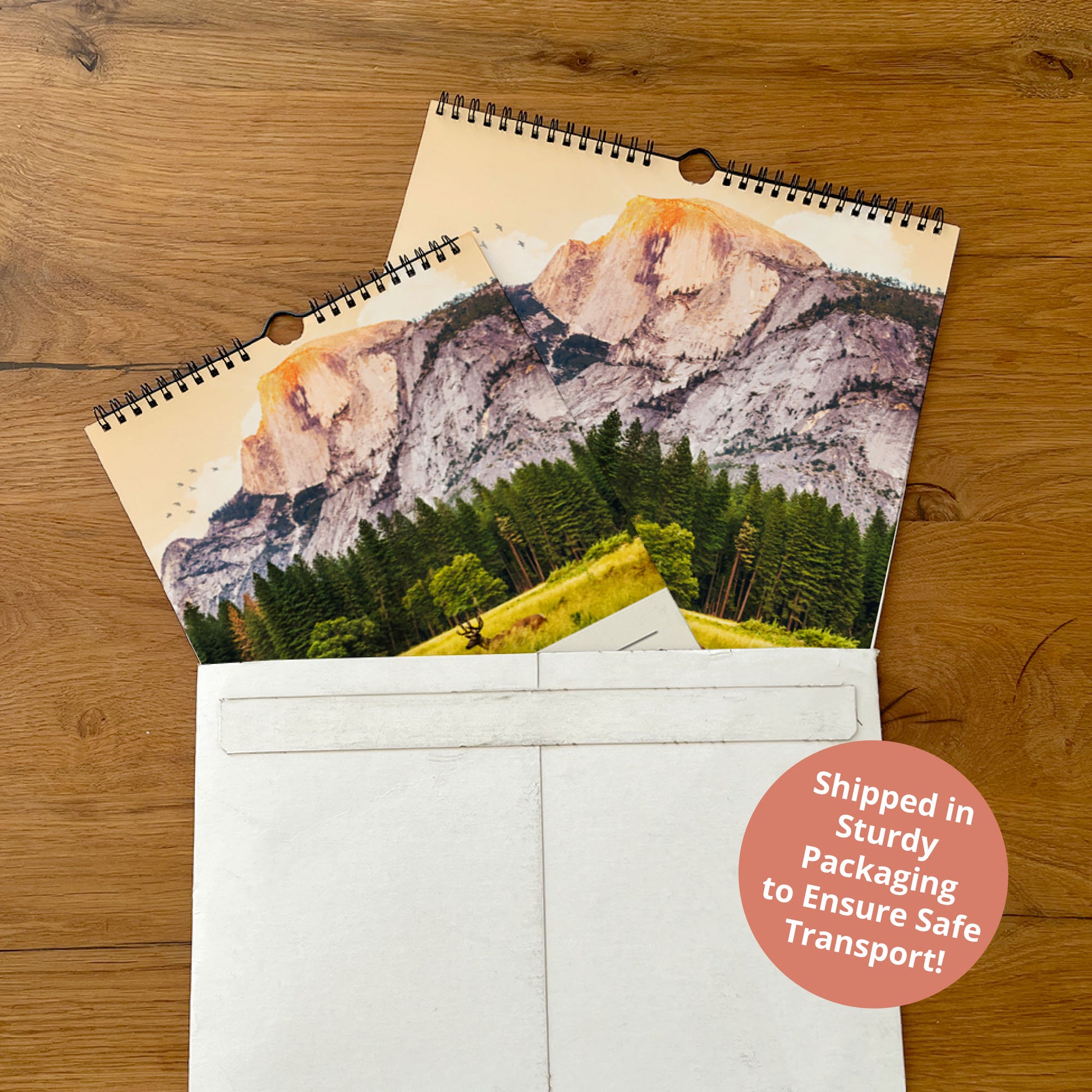 a wooden surface with two spiral-bound photo calendars, one with a mountain landscape and the other with a forest scene.
