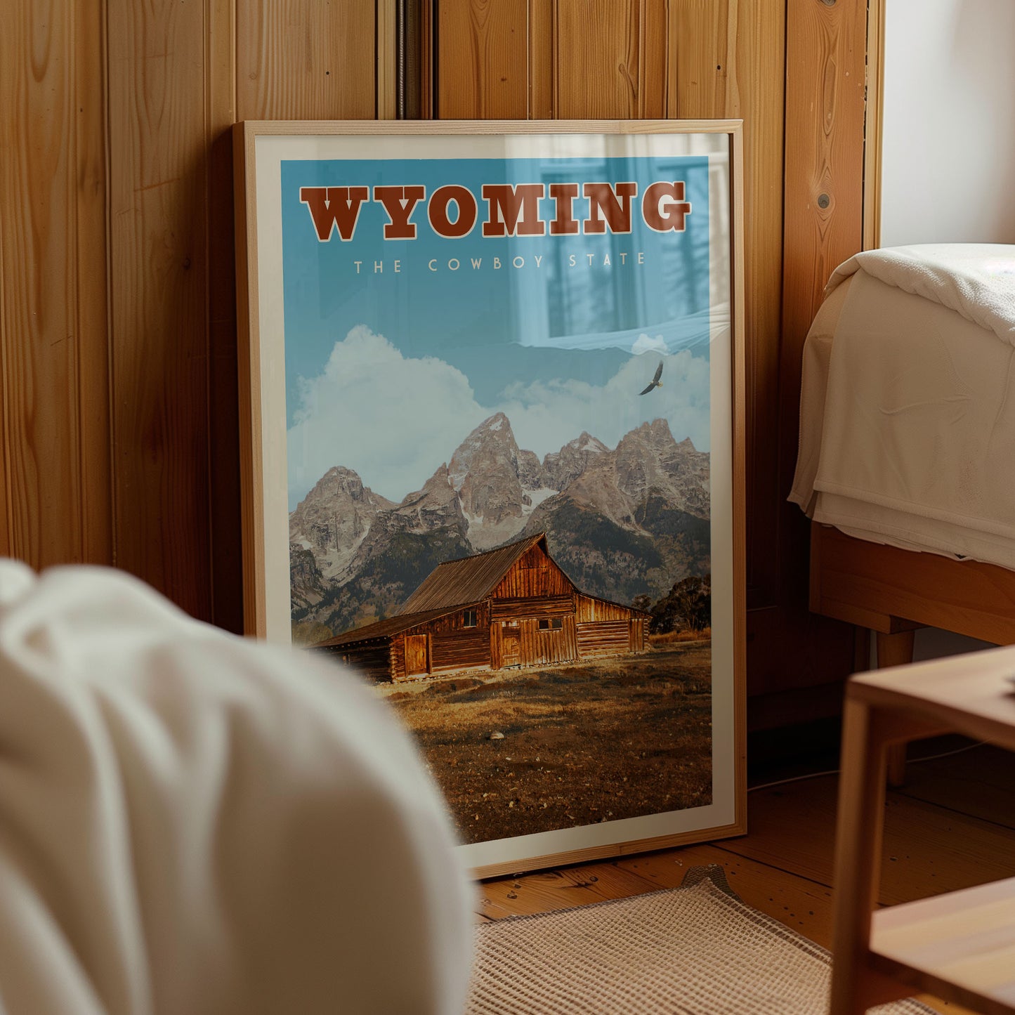 A framed poster of a cabin in the mountains, with the text "Wyoming" prominently displayed, is the central focus of the image.