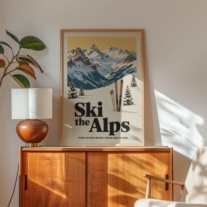 a framed poster of a snowy mountain landscape with skis, placed on a wooden cabinet or shelf.