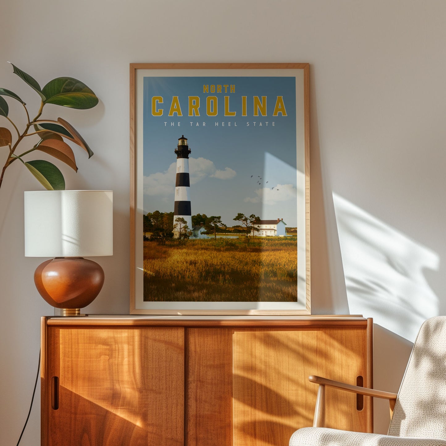 a framed poster of the Cape Hatteras Lighthouse in North Carolina, with a serene landscape of a lighthouse and a field in the background.